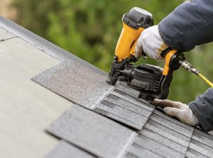 Roofer installing asphalt shingles on a residential roof using professional roofing tools