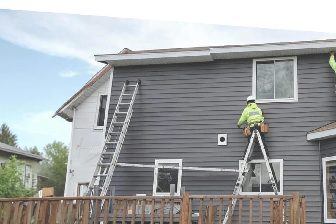 Siding contractor installing new exterior siding on a residential home using ladders and safety equipment