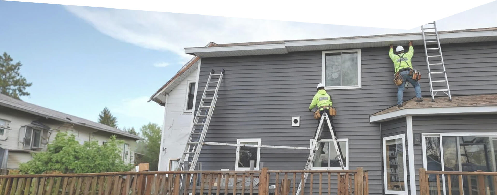 Siding contractor installing new exterior siding on a residential home using ladders and safety equipment